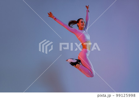 Smiling sporty woman in sportswear jumping on studio background. Sport and healthy lifestyle Smiling sporty woman in sportswear jumping on studio background. Sport and healthy lifestyle 99125998