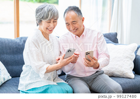 リビングでスマホを持つシニア夫婦 リビングでスマホを持つシニア夫婦 99127480