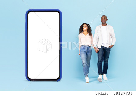 Great offer. African american couple walking near big smartphone with blank screen, promoting app or website, mockup 99127739