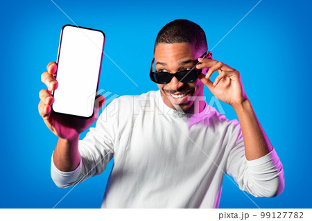 Stylish black man wearing sunglasses showing smartphone with empty screen 99127782