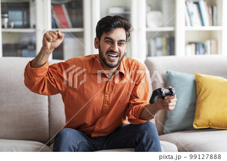 Cheerful arab guy enjoying his new video games set Cheerful arab guy enjoying his new video games set 99127888