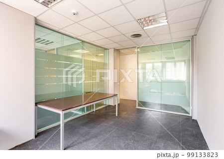 In a bankrupt office building, one of the many empty rooms with transparent, solid glass wall panels and an outdated ceiling covering is in need of repair and refurbishment. In a bankrupt office building, one of the many empty rooms with transparent, solid glass wall panels and an outdated ceiling covering is in need of repair and refurbishment. 99133823