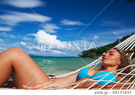 Woman laying in hammock on beach 99135695