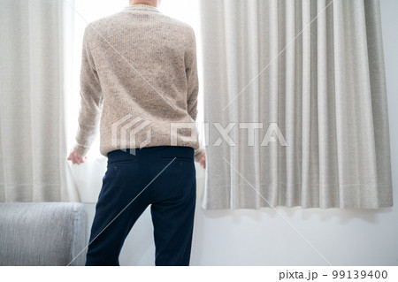 若い男性がリビングの窓から外を見る 若い男性がリビングの窓から外を見る 99139400