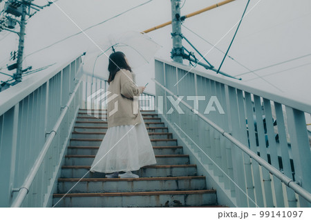 陸橋に傘をさしてスマホを持っている女性の写真 99141097