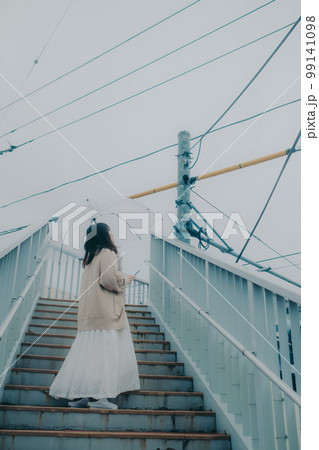 陸橋に傘をさしてスマホを持っている女性の写真 99141098
