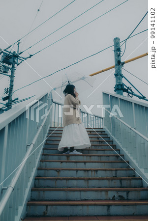 陸橋に傘をさしてスマホを持っている女性の写真 99141102