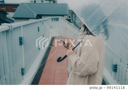 陸橋に傘をさしてスマホを持っている女性の写真 陸橋に傘をさしてスマホを持っている女性の写真 99141118