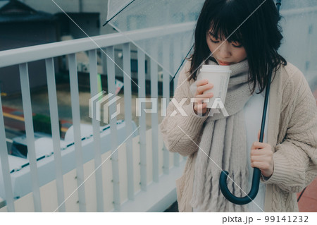 陸橋に傘をさしてコーヒーを飲んで待ち合わせをしている女性の写真 99141232