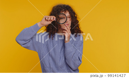 Investigator researcher woman with magnifying glass near face, looking into camera with big zoom eye Investigator researcher woman with magnifying glass near face, looking into camera with big zoom eye 99141427