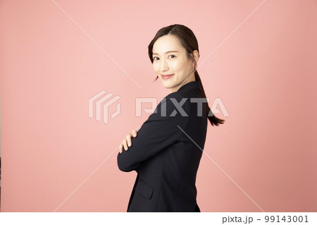 ピンクバックで腕を組んで振り向いて微笑む女性 99143001