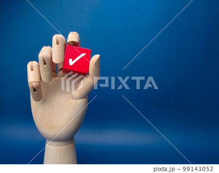 Wooden hand holding red cube with correct sign on blue background. Business concept. 99143052