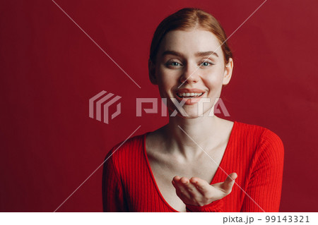 Portrait of beautiful young redhaired woman blowing kisses over red background. 99143321
