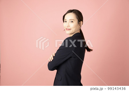 ピンクバックで腕を組んで振り向いて微笑む女性 99143436