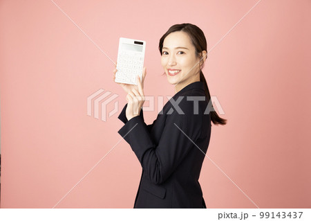 ピンクバックでネイビーのスーツを着て白い電卓を持つ女性 ピンクバックでネイビーのスーツを着て白い電卓を持つ女性 99143437
