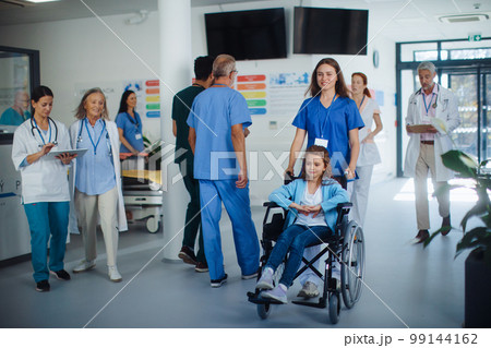 Young nurse pushing little girl on wheelchair at hospital corridor. Young nurse pushing little girl on wheelchair at hospital corridor. 99144162