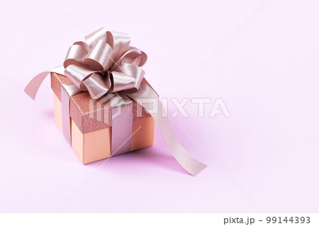 Lilac festive gift box with a satin ribbon bow on a lilac background. Happy Valentine's Day, Mother's Day and birthday greeting card. 99144393