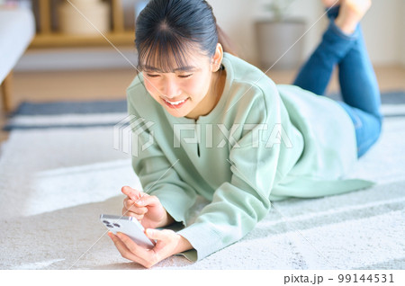 明るい部屋でスマホを操作する笑顔の若い女性 明るい部屋でスマホを操作する笑顔の若い女性 99144531