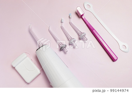 Oral hygiene set. Oral teeth irrigator with nozzle pack, toothbrush, dental floss, tongue scraper. Top view, pink background Dental care, treatments, daily routine. Horizontal , closeup 99144974