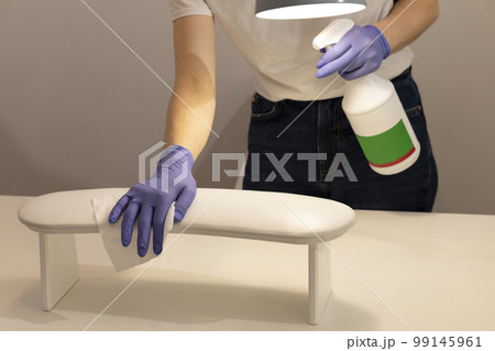 Cropped Manicure technician cleans, sanitizes tools, equipment, maintains workstation, treatment room. White manicurist works in gloves, holds isopropyl alcohol spray bottle, soapy water. Horizontal 99145961