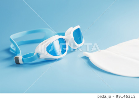 White swimming glasses in hand on a blue background with a white cap White swimming glasses in hand on a blue background with a white cap 99146215