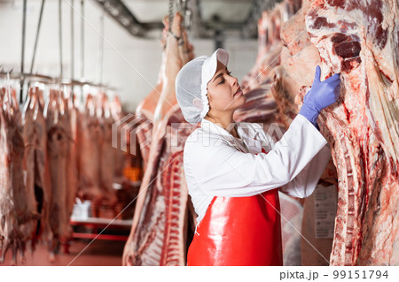 Female butcher showing beef chunk in meat storage 99151794