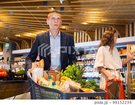 Shopper with shopping cart selects vegetables at grocery supermarket 99152234