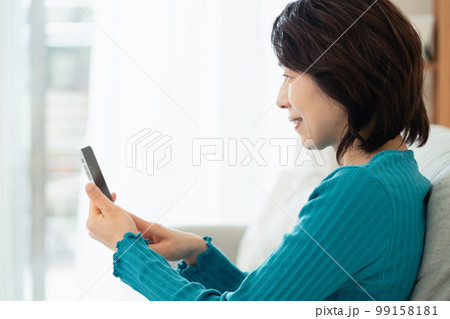 リビングでスマホを操作するミドル女性 99158181