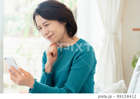 リビングでスマホを見るミドル女性 99158412