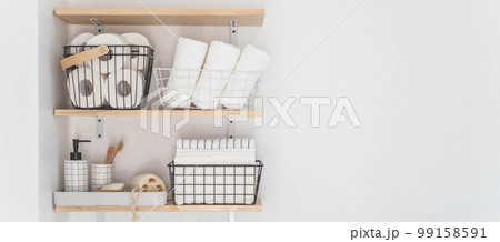 Beautiful white bathroom. Wooden shelves. Rolled towels, stacked towels and baskets. Soap, washcloth 99158591