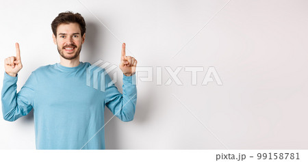 Image of young modern guy with beard showing advertisement on copy space, pointing fingers up and smiling, check it out gesture, white background Image of young modern guy with beard showing advertisement on copy space, pointing fingers up and smiling, check it out gesture, white background 99158781