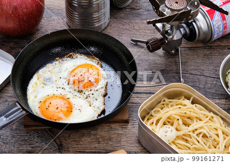 木製のテーブルの上の目玉焼きやスパゲッティのキャンプ飯 99161271