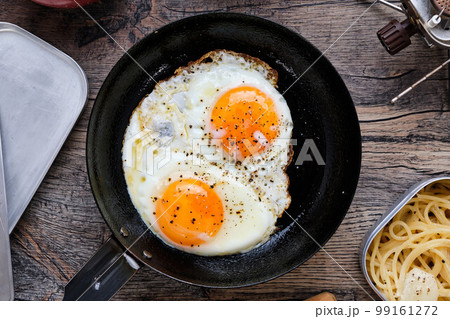 木製のテーブルの上の目玉焼きやスパゲッティのキャンプ飯 99161272