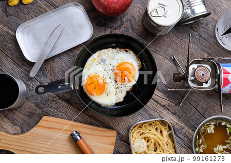 木製のテーブルの上の目玉焼きやスパゲッティのキャンプ飯 99161273