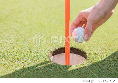 ゴルフ場のカップからゴルフボールを取り出すゴルファー 99162912