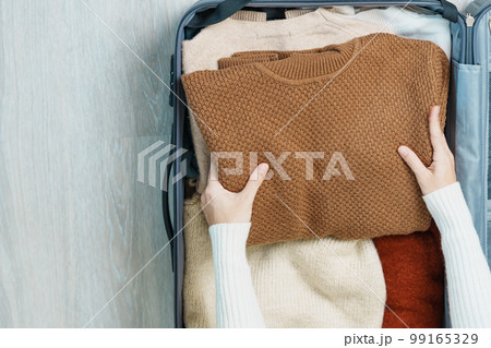 Woman hand packing her winter clothes in luggage. Time to travel, trip, Relax, spring or autumn or winter season and vacation concepts Woman hand packing her winter clothes in luggage. Time to travel, trip, Relax, spring or autumn or winter season and vacation concepts 99165329