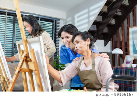 senior painting in art class with friends from her care home for the aged copying a painting with water colors in retirement home. 99166167