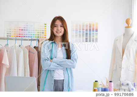 A young asian female fashion designer is standing with arms folded confident and looking at camera in her design studio. 99170686