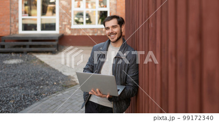 young man with a laptop in his hands smiling looking at the camera outside young man with a laptop in his hands smiling looking at the camera outside 99172340