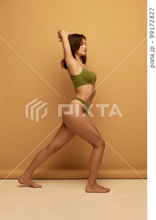 Portrait of young slim beautiful girl wearing green color underwear posing over brown background. Concept of beauty, body and skin care, healthy eating Portrait of young slim beautiful girl wearing green color underwear posing over brown background. Concept of beauty, body and skin care, healthy eating 99172827