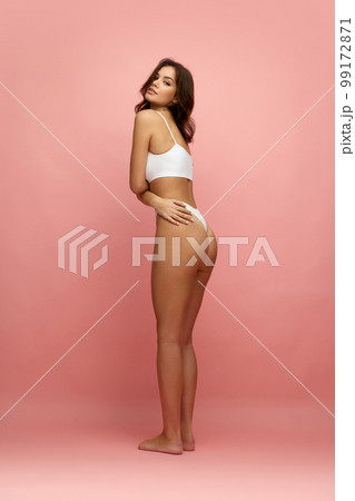Beautiful sensual slender girl with long soft brown hair wearing white inner wear posing over pink background. Concept of natural beauty, body and skin care, healthy eating Beautiful sensual slender girl with long soft brown hair wearing white inner wear posing over pink background. Concept of natural beauty, body and skin care, healthy eating 99172871