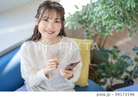 ソファでスマホを操作する若い女性 99173596