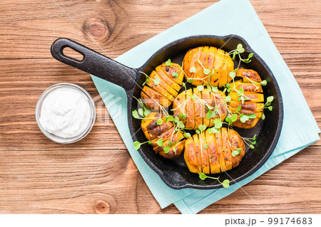 Baked young potatoes in spices and oil with arugula in a iron pan on a wooden table. Top view 99174683
