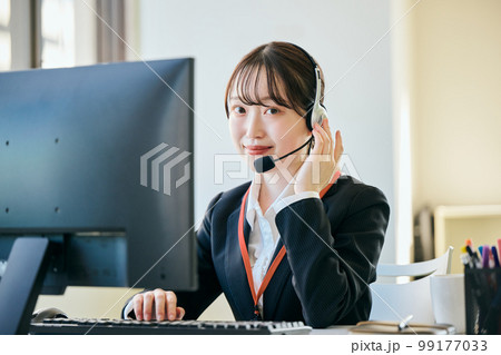 オフィスで電話対応をするカメラ目線の若い女性 99177033