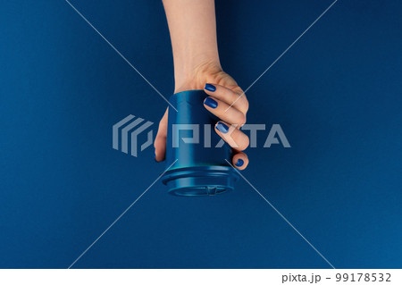 Female hand holding takeaway coffee cup gainst classic blue background Female hand holding takeaway coffee cup gainst classic blue background 99178532