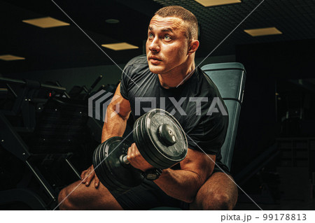 Muscular young man lifting weights in a dark gym Muscular young man lifting weights in a dark gym 99178813