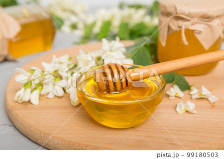 Sweet honey jar surrounded spring acacia blossoms. Honey flows from a spoon in a jar. jars of clear fresh acacia honey on wooden background 99180503