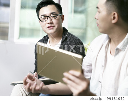 two young asian entrepreneurs discussing business in office using digital tablet 99181052