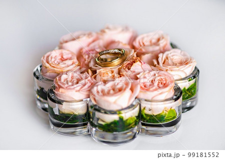 Wedding gold rings with diamonds on pink roses in a glass holder. 99181552