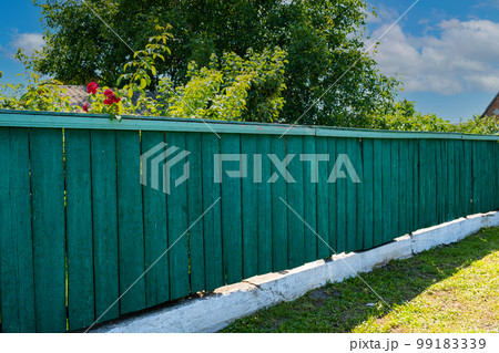 The old weathered wooden green fence near residential homes. 99183339